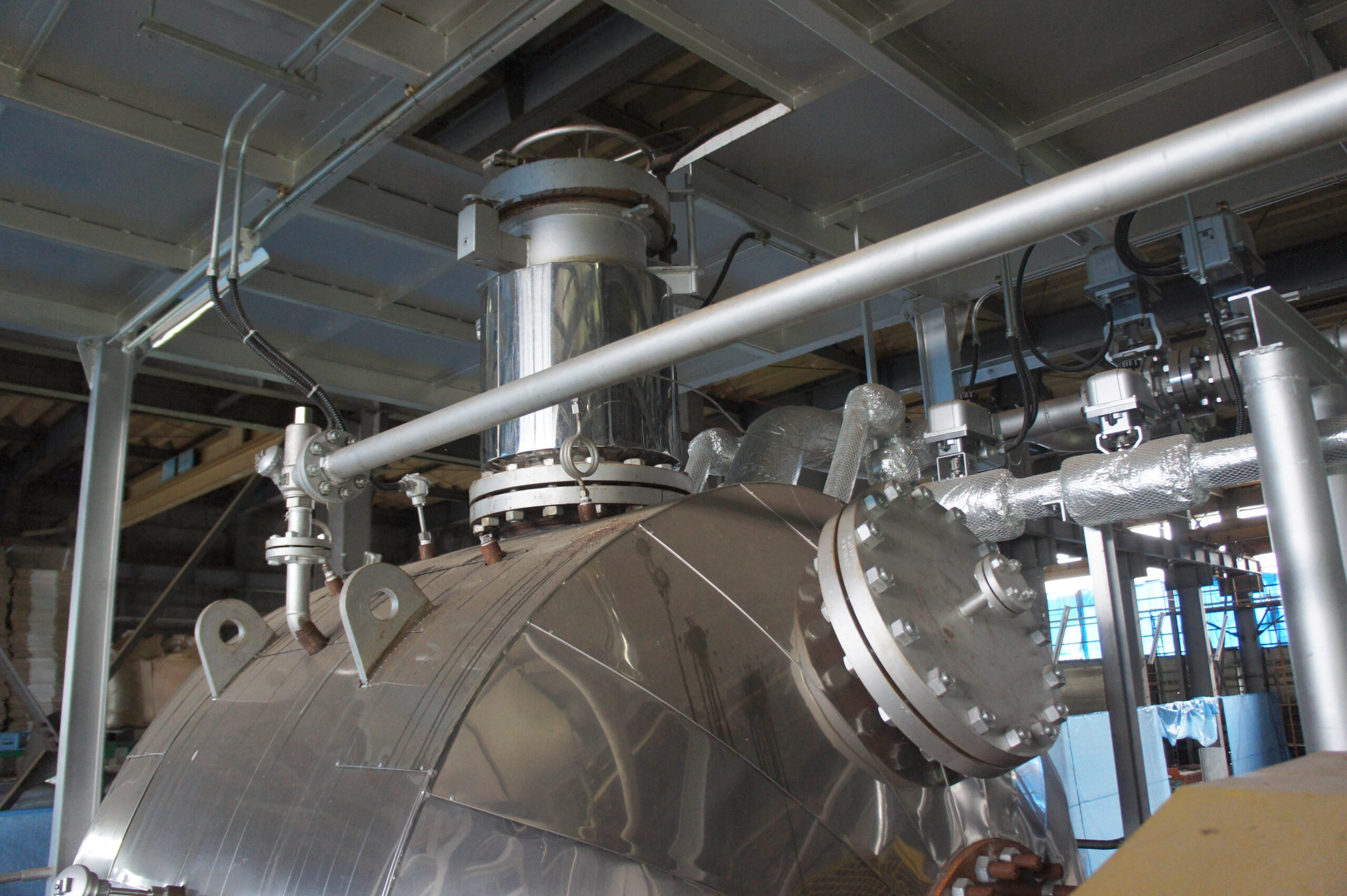 Industrial stainless-steel machinery with connected piping and valves inside a factory